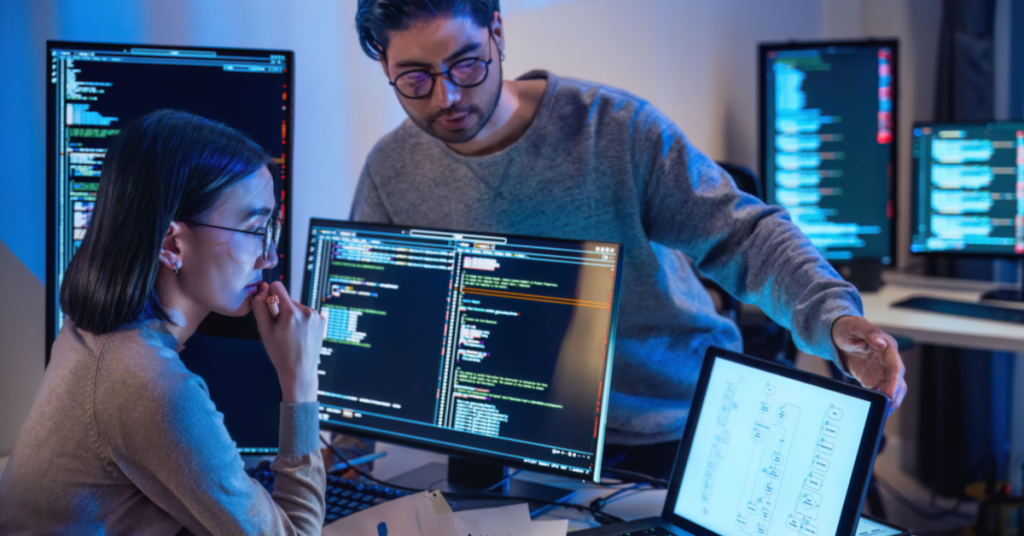Two professionals collaborating on AI and prompt engineering at a workspace with multiple computer screens.
